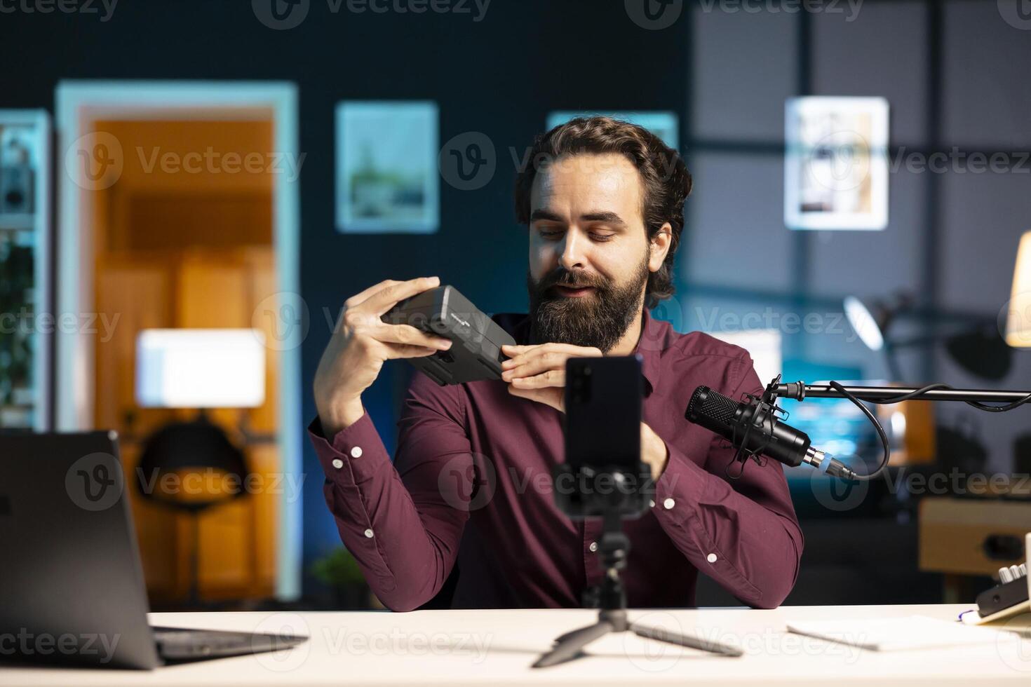 Tech expert presenting features of newly launched V mount battery, filming technology review using smartphone on tripod. Reviewer showcasing charging device specs, recording with phone photo