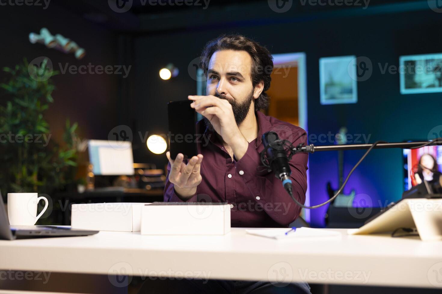 Tech guru reviewing latest mobile phone, filming internet show in neon lights studio, shooting technology vlog using professional microphone. Content creator presenting best smartphones on the market photo