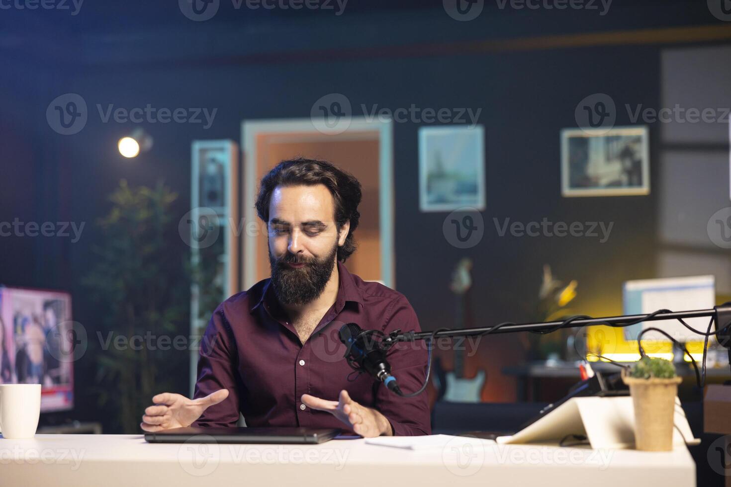 Man in studio endorsing laptop from brand sponsoring , talking in professional microphone. Content creator does influencer marketing by promoting notebook, recording with high tech mic photo