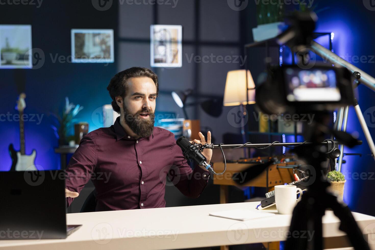 Influencer talking in professional microphone in studio illuminated with rgb lights at night, filming internet production. Man uses content creation recording mic in apartment photo