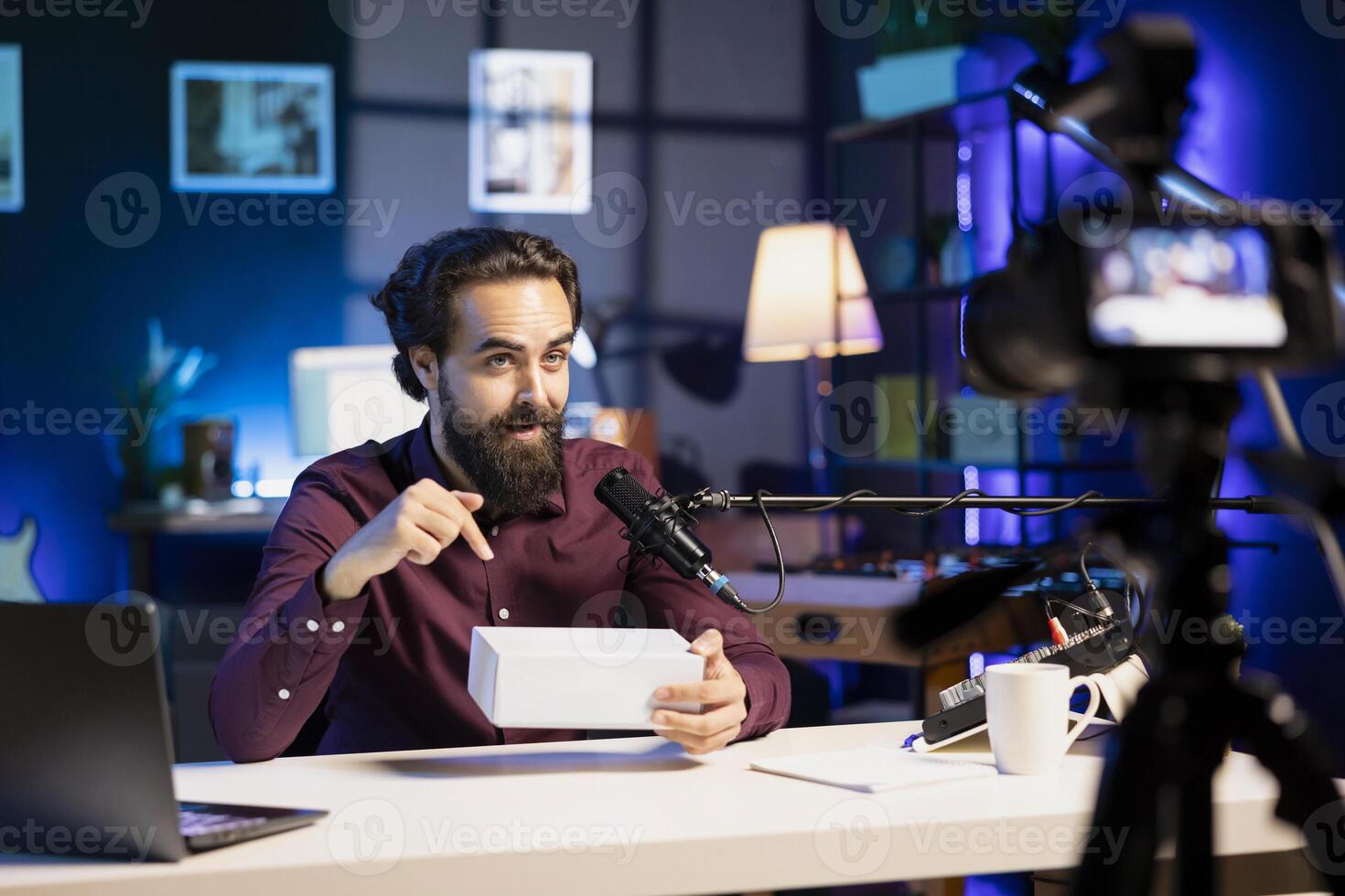 Content creator receiving mystery box from subscribers, ready to film packaged product unboxing. Internet star pointing to surprise package received, recording in home studio photo