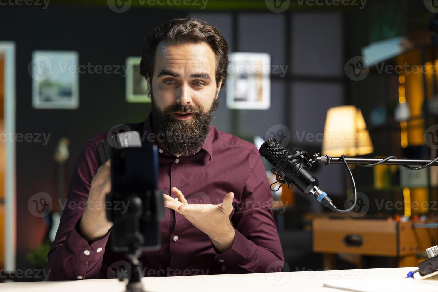 Tech guru presenting V mount battery, filming technology review using cellphone on tripod and professional microphone. Caucasian vlogger showcasing charging device specs, recording with phone photo