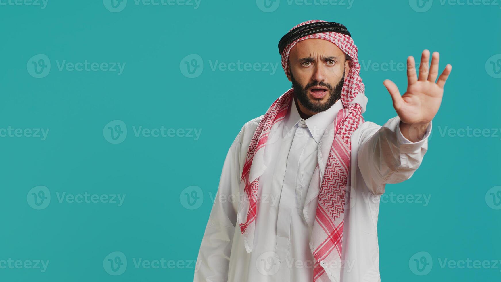 Middle eastern guy doing stop gesture with palm, expressing negativity and refusal in studio. Young male model presenting rejection, being disappointed with stuff over backdrop. photo