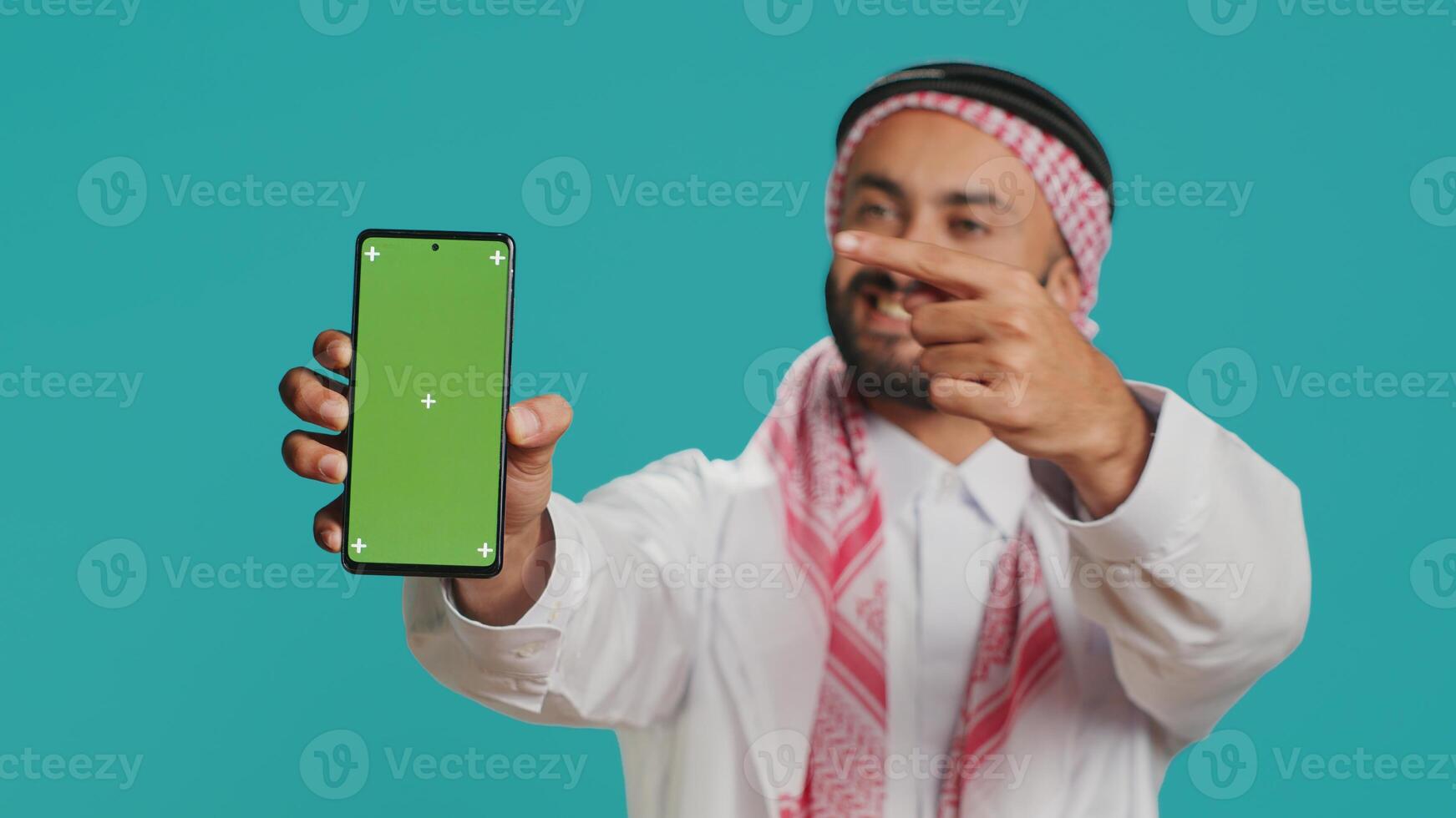 Muslim man on mobile device with greenscreen theme, Putting forward isolated mockup chromakey on smartphone display. Young arabic person exhibits blank copyspace template design. photo