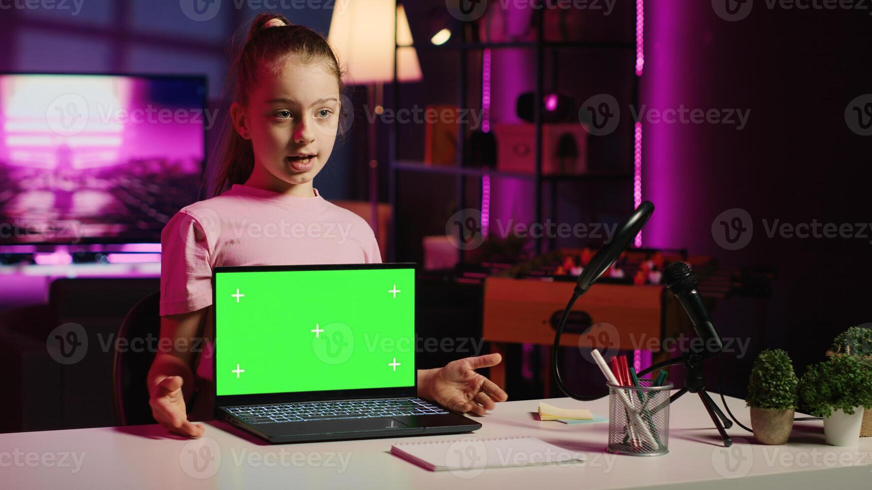 Kid influencer in home studio using recording gear to record review of mockup laptop. Young girl online show host filming electronics haul, presenting isolated screen notebook for viewers photo