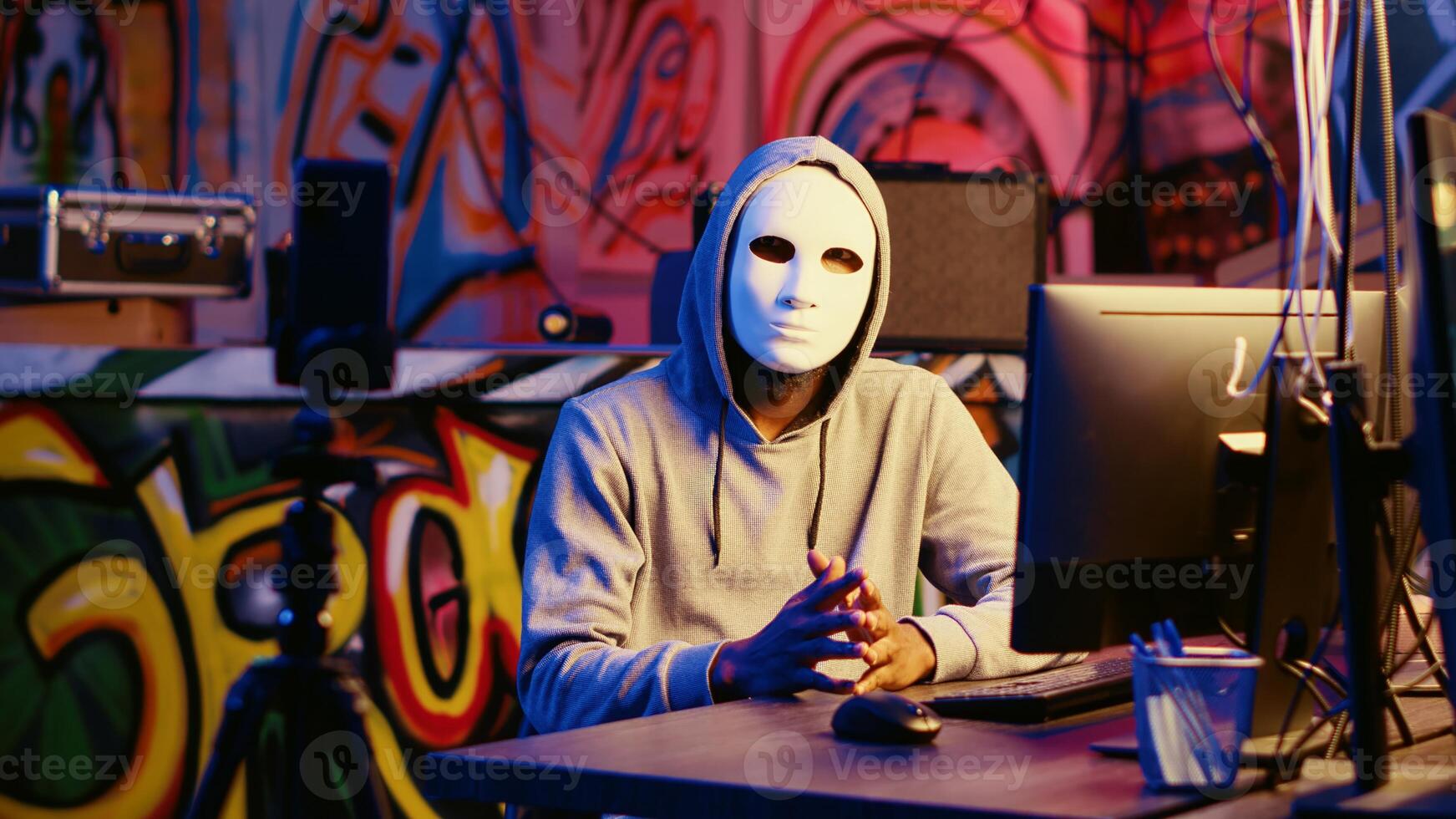 Anonymous masked dissident hacker filming anti government message, fighting against propaganda. Hooded social justice crusader using smartphone to record threatening photo