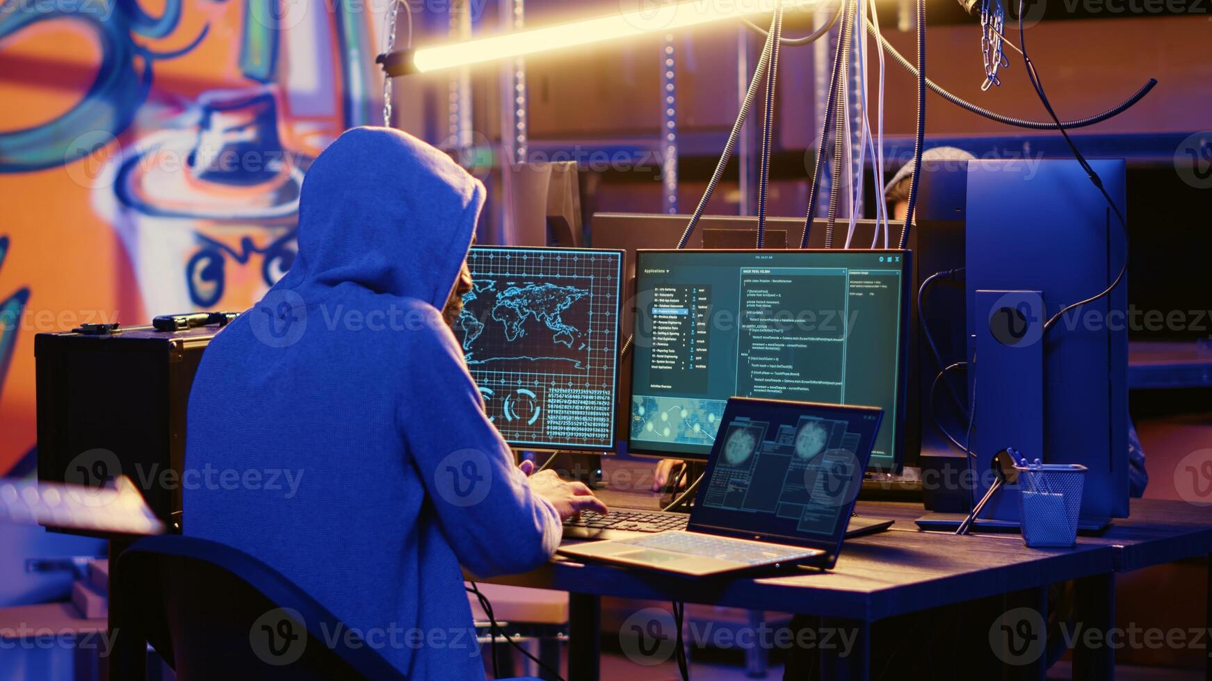 Hacker in abandoned warehouse with graffiti walls writing code that spoofs his location, tricking cops. Rogue developer running script on many devices pinging wrong location to cybercriminal police photo