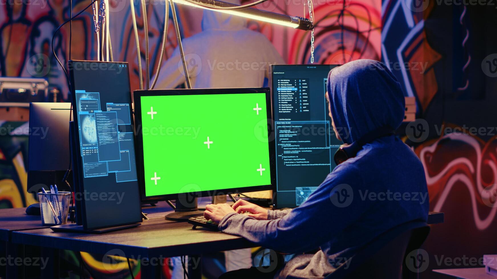 Hackers using green screen PC to code malware designed to exploit network backdoors. Cybercriminals use mockup monitor while bypassing security measures in graffiti painted bunker photo