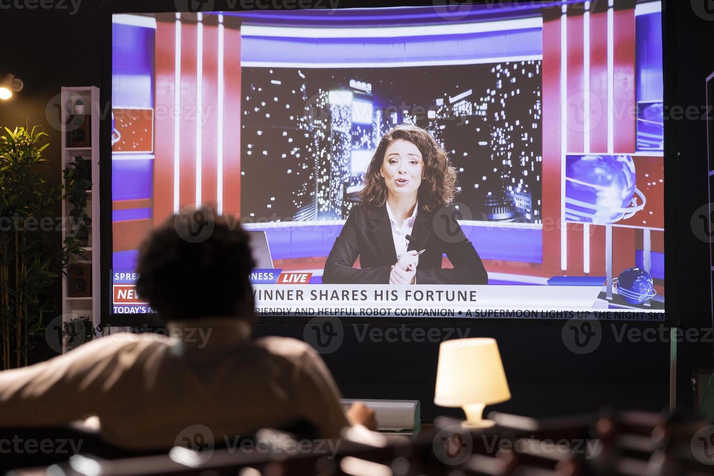Cord cutter sitting on couch in front of widescreen smart TV displaying streamed news program. Person watching big television screen showing on demand channel with newscast coverage photo