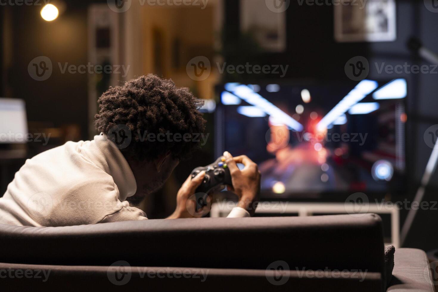 Man holding controller in apartment, playing videogames on smart TV display. Gamer on couch using joystick to participate in PvP online multiplayer game on console system attached to television set photo