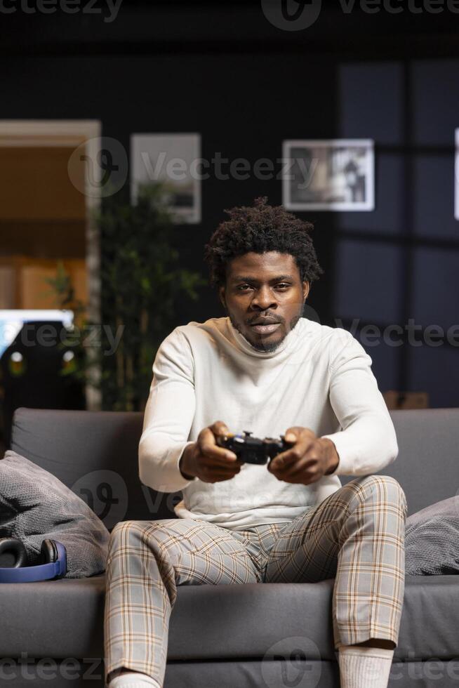 African american player using controller to play videogames on smart TV, enjoying leisure time in living room. Man in home theatre using gaming console joystick to complete levels in singleplayer game photo