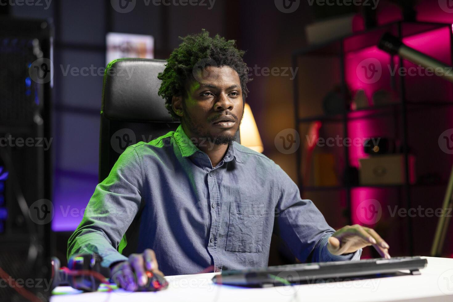 African american man in apartment playing videogames on gaming PC at computer desk all day, feeling tired. Gamer strained and exhausted after contending against rival players in esports multiplayer game photo