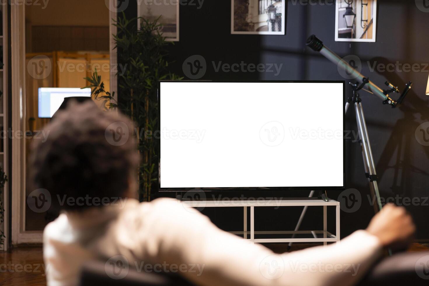BIPOC man lounged on cozy couch, watching news broadcast on mockup smart TV while relaxing in apartment. Homeowner streaming on demand broadcast program on isolated screen television set photo