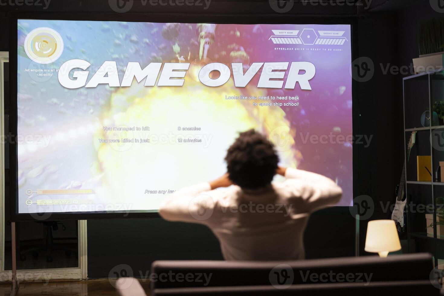 Gamer upset at seeing game over message on ultrawide TV screen playing arcade space shooter videogame. Man spending time at home on gaming system, frustrated after losing online competition photo