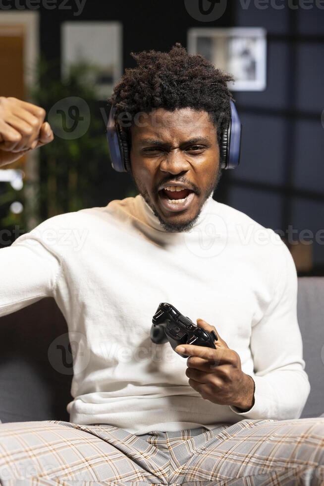Gamer feeling relieved after winning videogame level, screaming at television set in excitement. Pleased man at home yelling from joy after seeing achieving victory while playing on gaming console photo