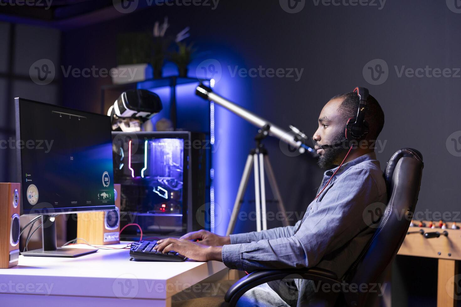 Man in RGB lit apartment playing immersive games on desktop PC at computer desk, unwinding after work. African american gamer competing against enemies in internet multiplayer shooter photo