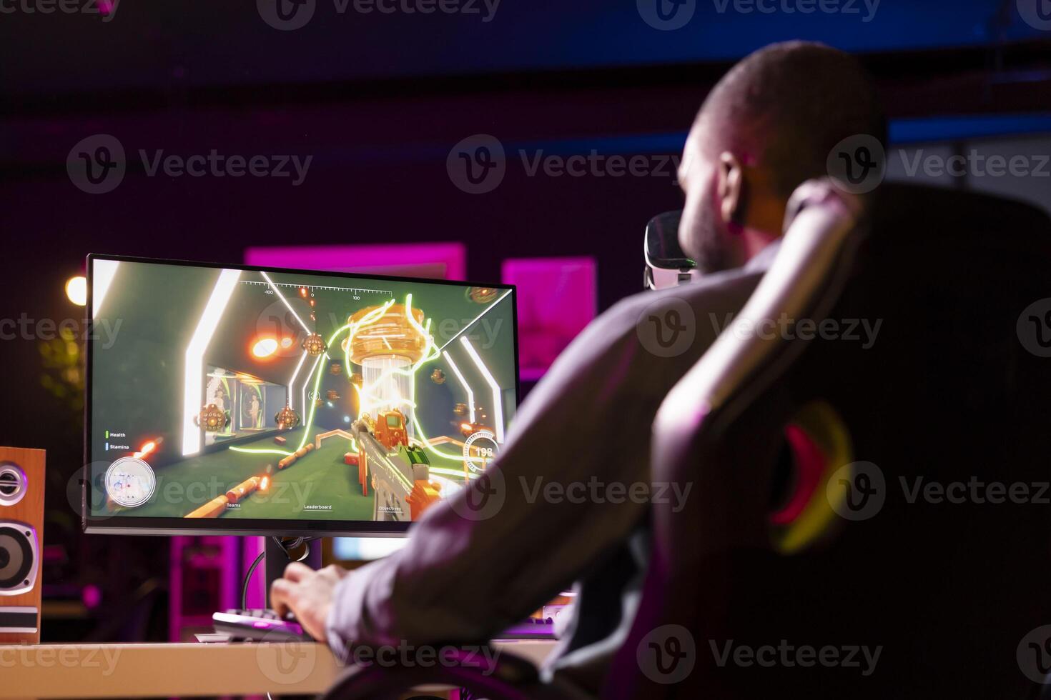 Man in neon lit apartment playing immersive games on gaming PC at computer desk, unwinding after work. Gamer competing against enemies in internet multiplayer shooter photo