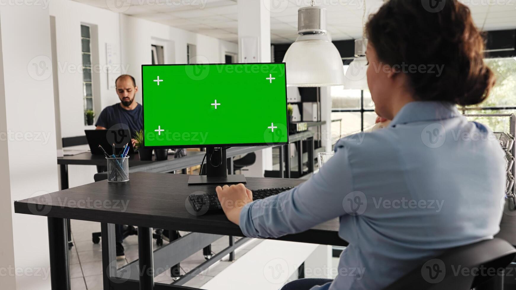 Employee sitting at desk with greenscreen on monitor, looking at isolated copyspace layout on computer desktop in coworking space. Businesswoman working on pc, blank mockup template. photo