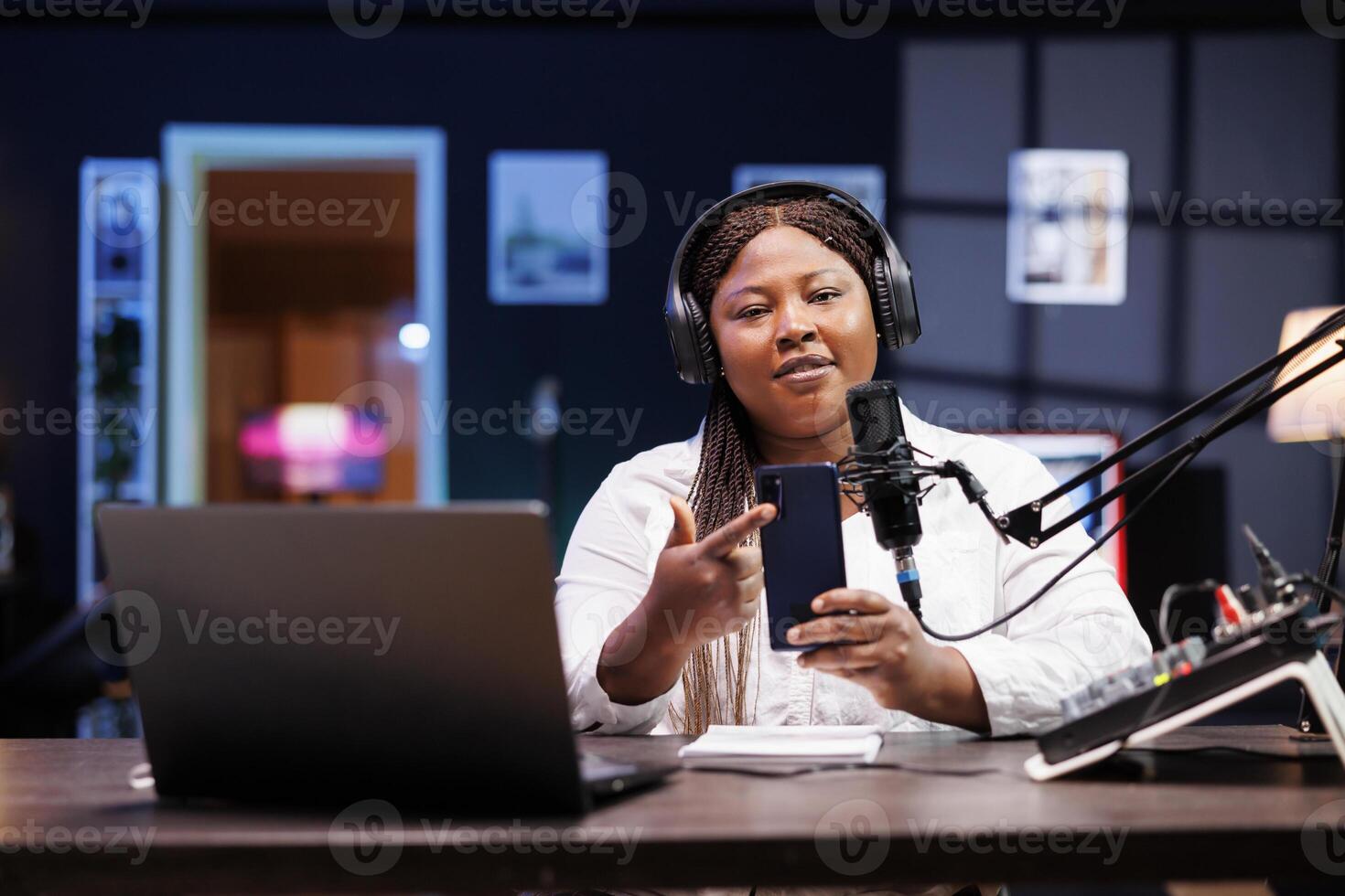 Promoting a recently released cellphone for social media platforms is female influencer. Black woman describes her new mobile device while seated at the table and speaking into a microphone. photo