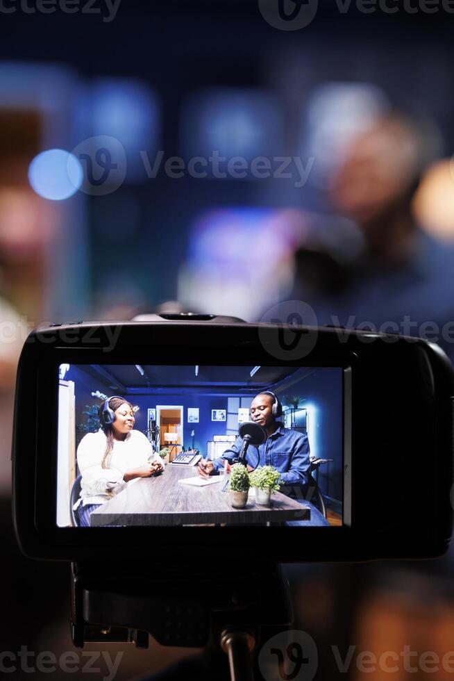 Selective focus on professional camera screen recording bloggers streaming live internet radio using microphones from home studio. Black couple filming vlog for social media platform photo