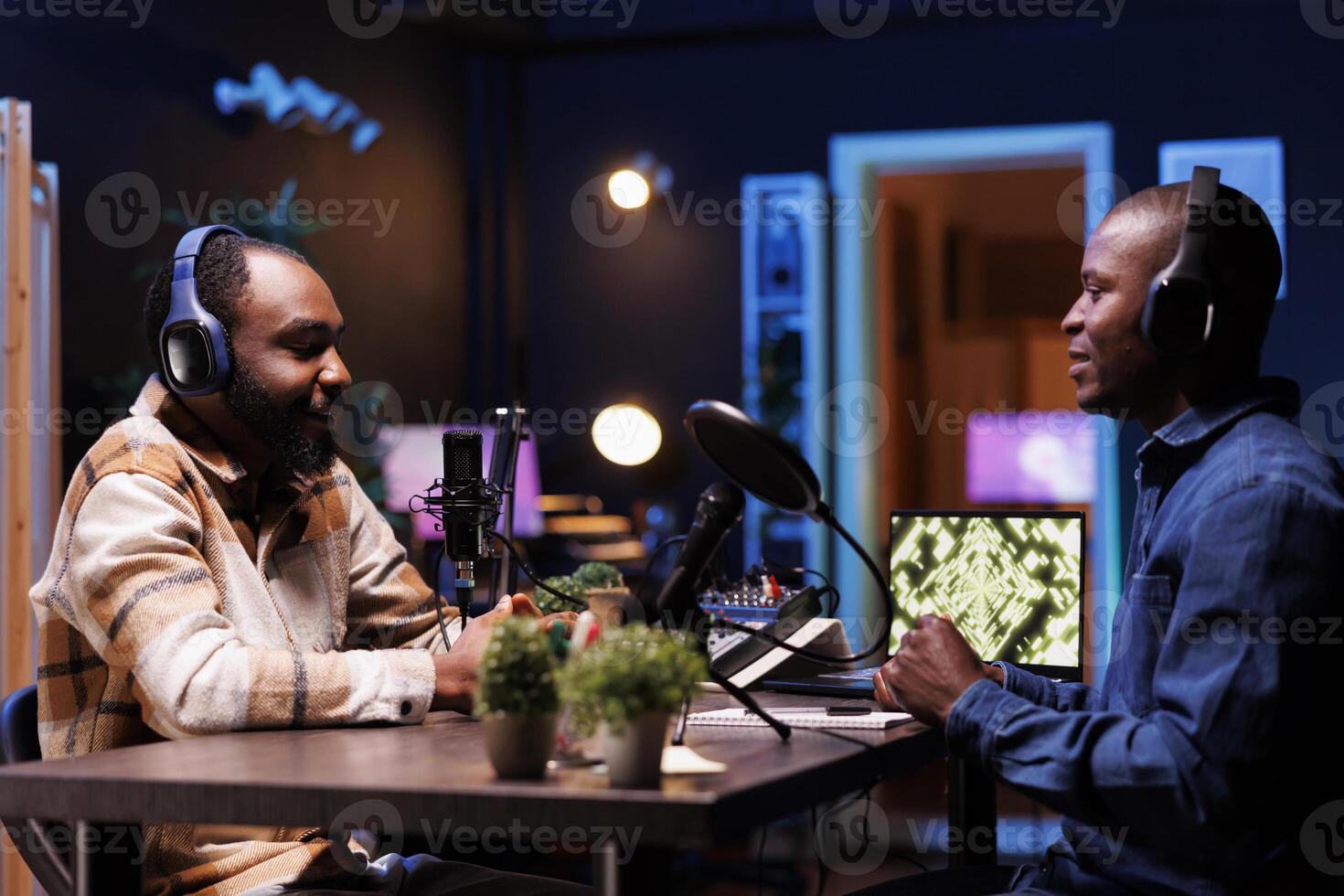 Young influencer uses audio recording equipment in his home studio to produce a podcast featuring a male guest. Happy african american men chit-chatting live during an internet show broadcast. photo