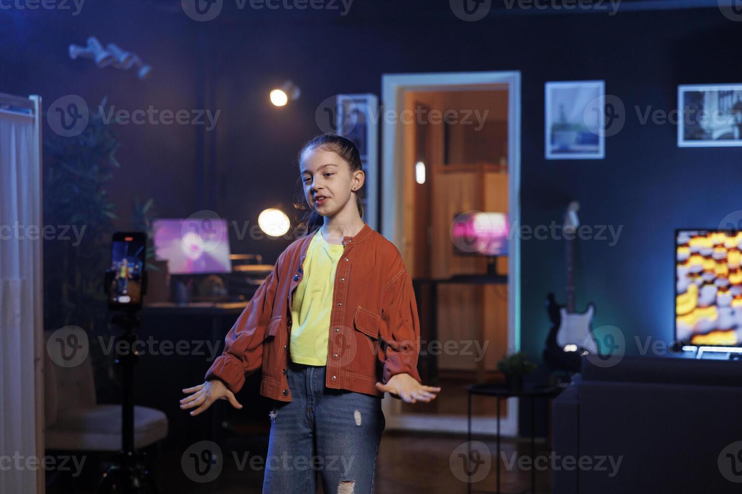 Girl dancing and singing while shooting with cellphone on tripod stabilizer for social media. Smiling kid entertains fans with professional choreography recorded with mobile phone photo