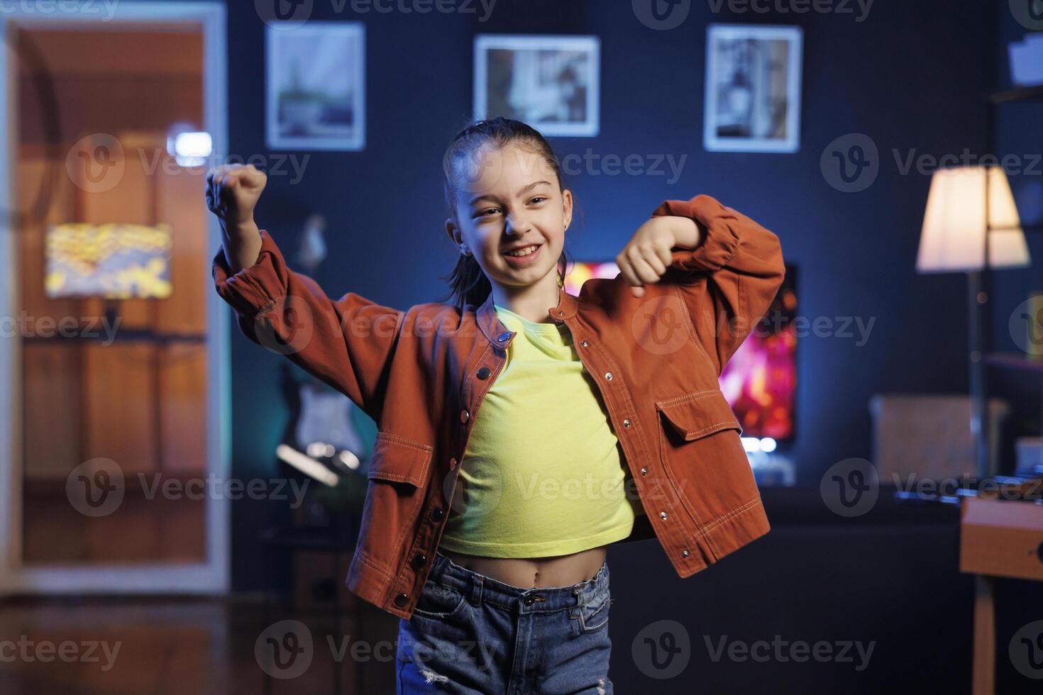 Pretty little girl dancing and singing while shooting for social media networks in home interior background. Child entertaining audiences with professional choreography photo