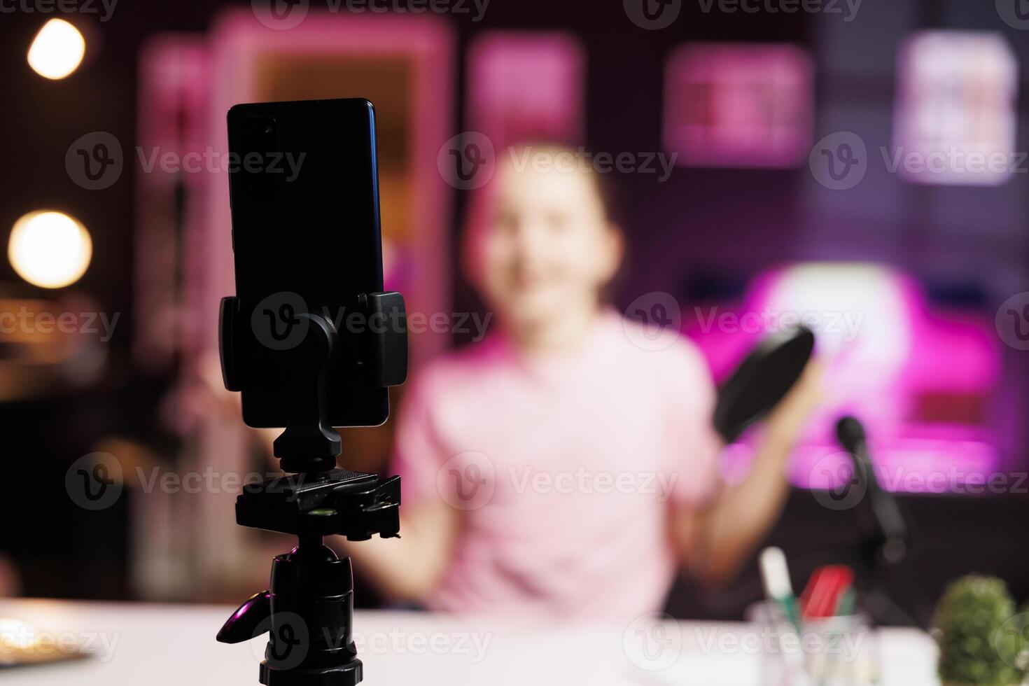 Close up shot of professional recording smartphone camera used by gen Z internet star to do livestream. Focus on production gear used by cute kid in blurry background to do live broadcast photo