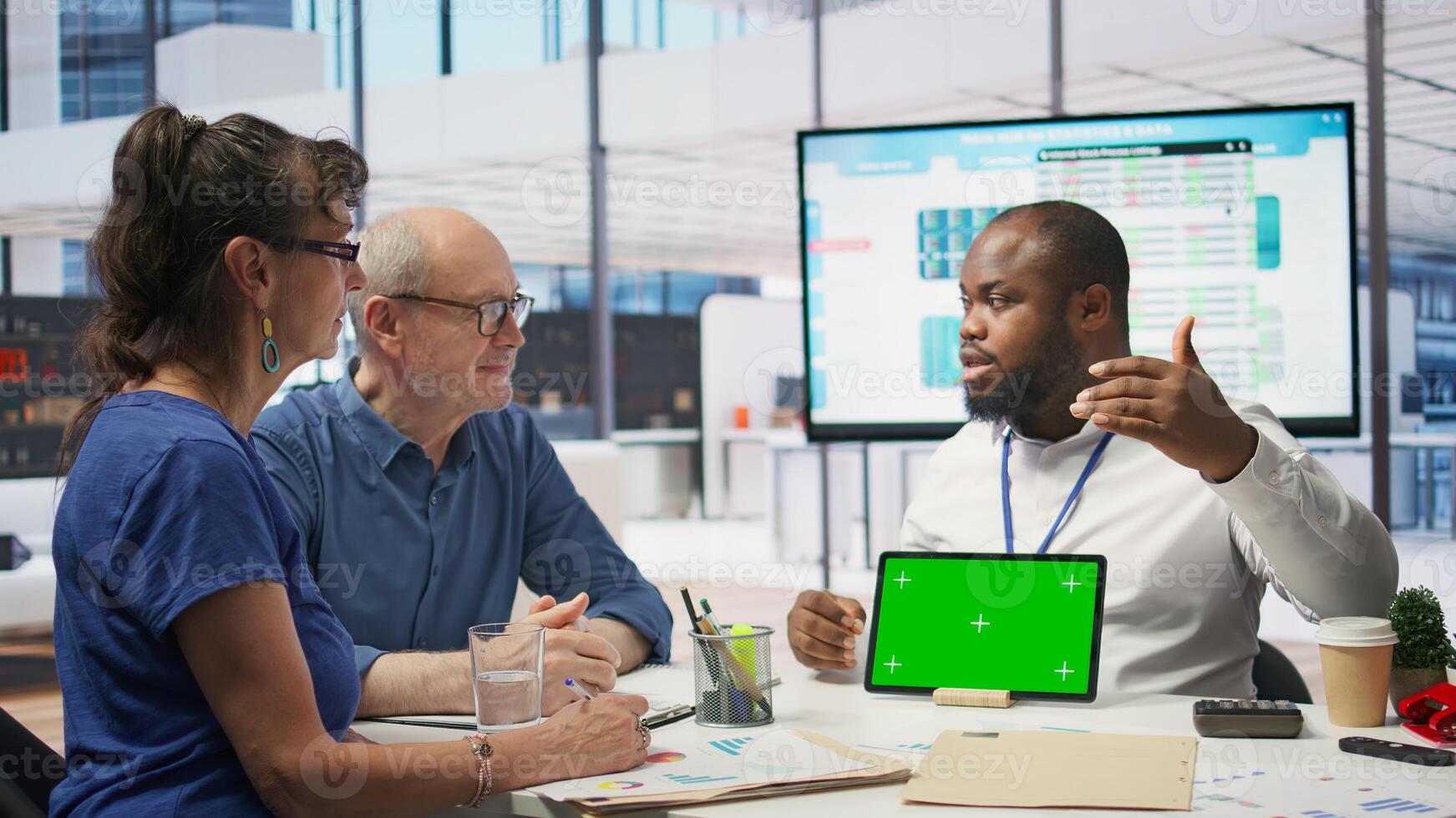 Expert shows tablet with mockup chroma key to mature couple in office, meeting for a counseling session about retirement plan options. Advisor helping senior people with their money. Camera B. photo
