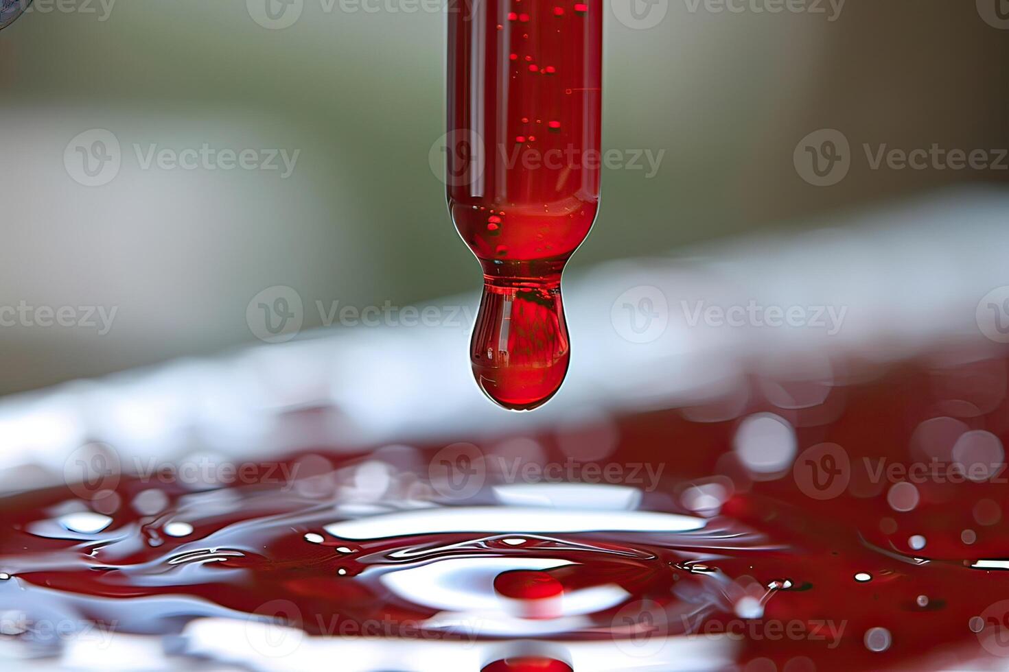 A drop of red liquid is being poured from a pipette onto a surface photo