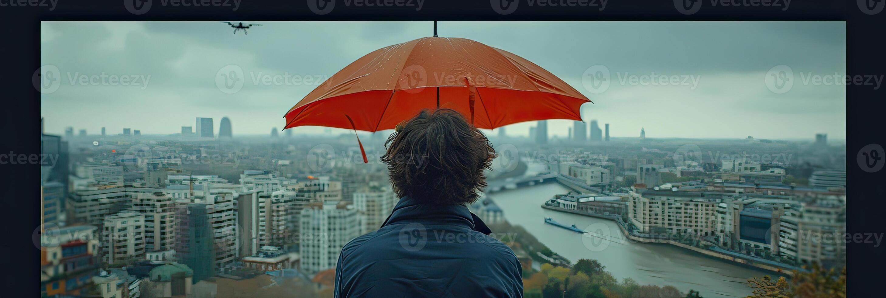 A man standing with a red umbrella, gazing at the city below on a beautiful day photo