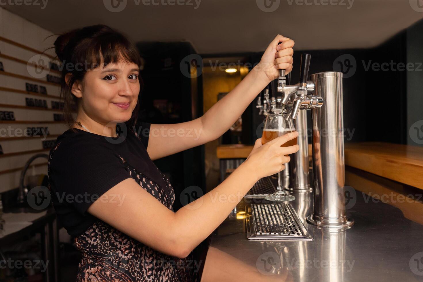 Portrait of waitress in profile filling a glass of beer from the tap. photo
