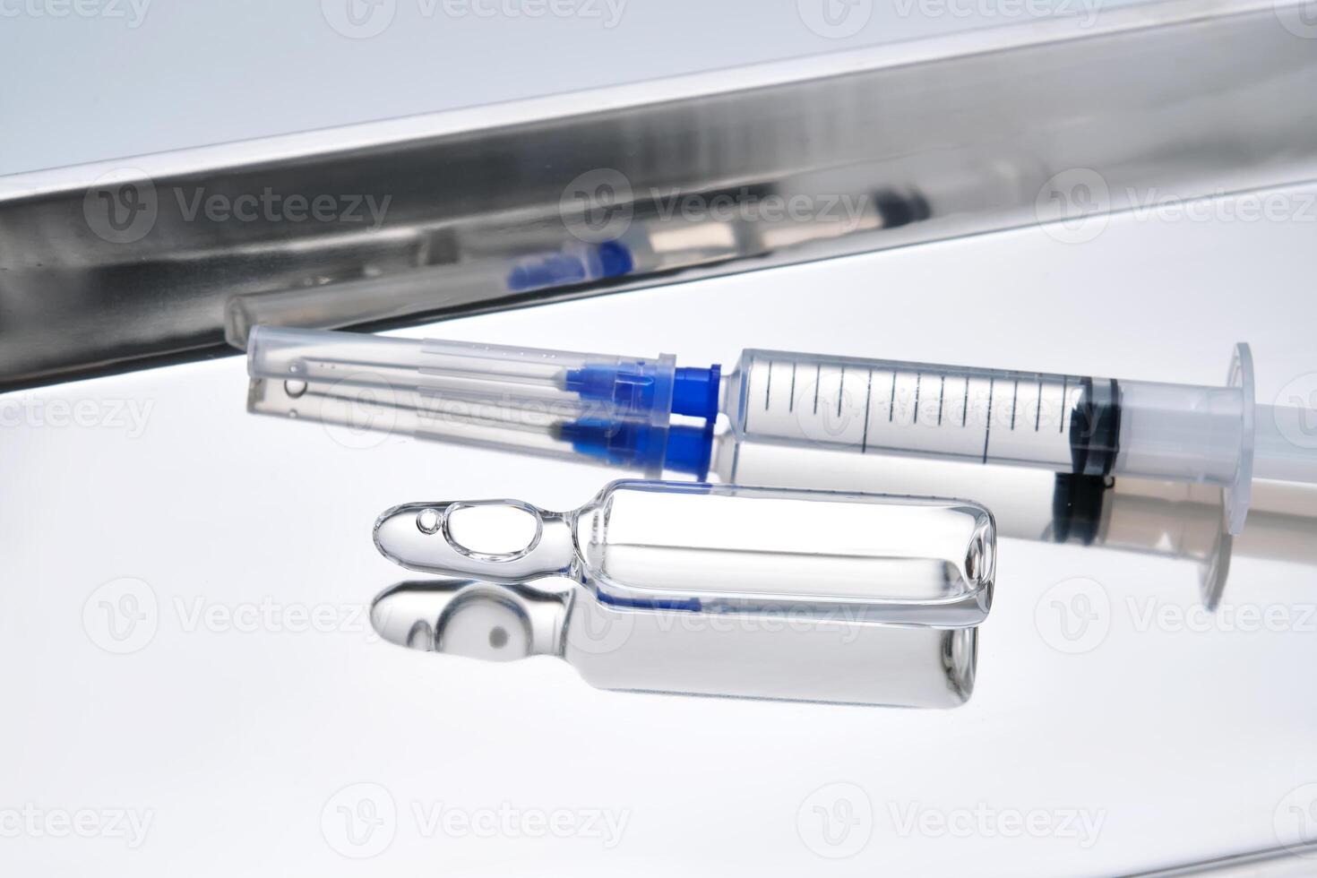 Syringes with needles and an ampoule in a stainless steel medical tray. photo