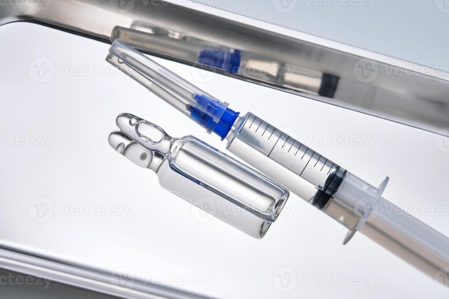 Syringes with needles and an ampoule in a stainless steel medical tray. photo