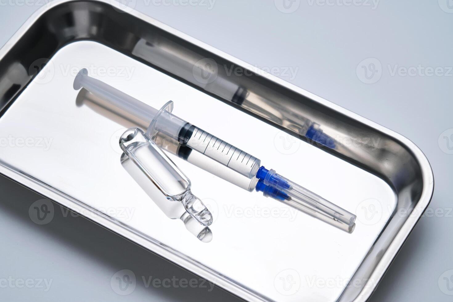 Syringes with needles and an ampoule in a stainless steel medical tray. photo