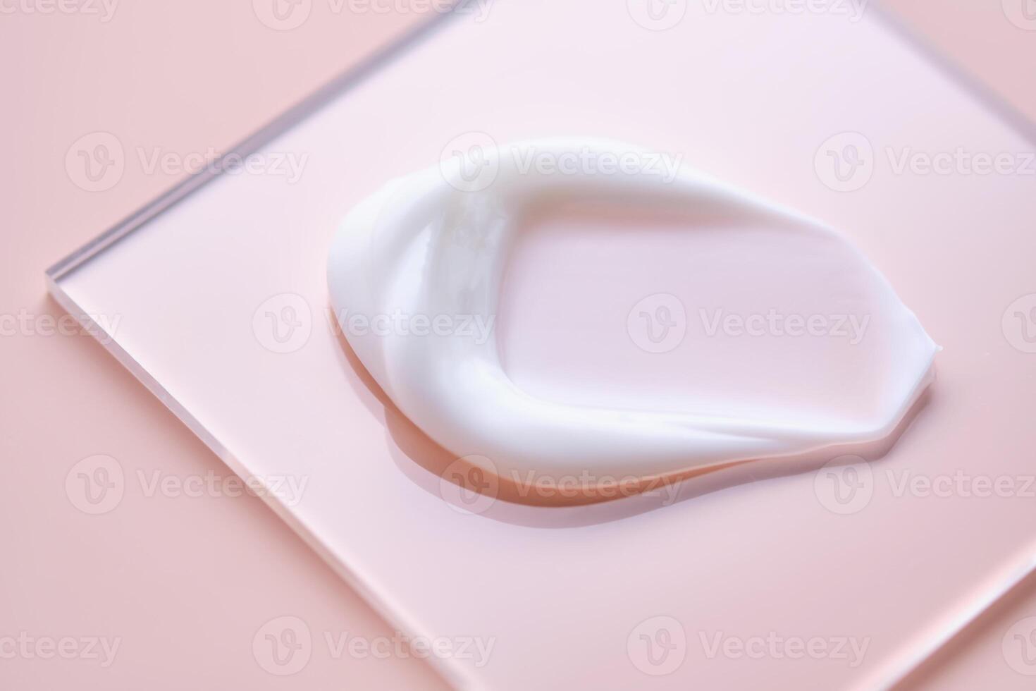 A smear of white cream on a square transparent stand on a pink background. photo