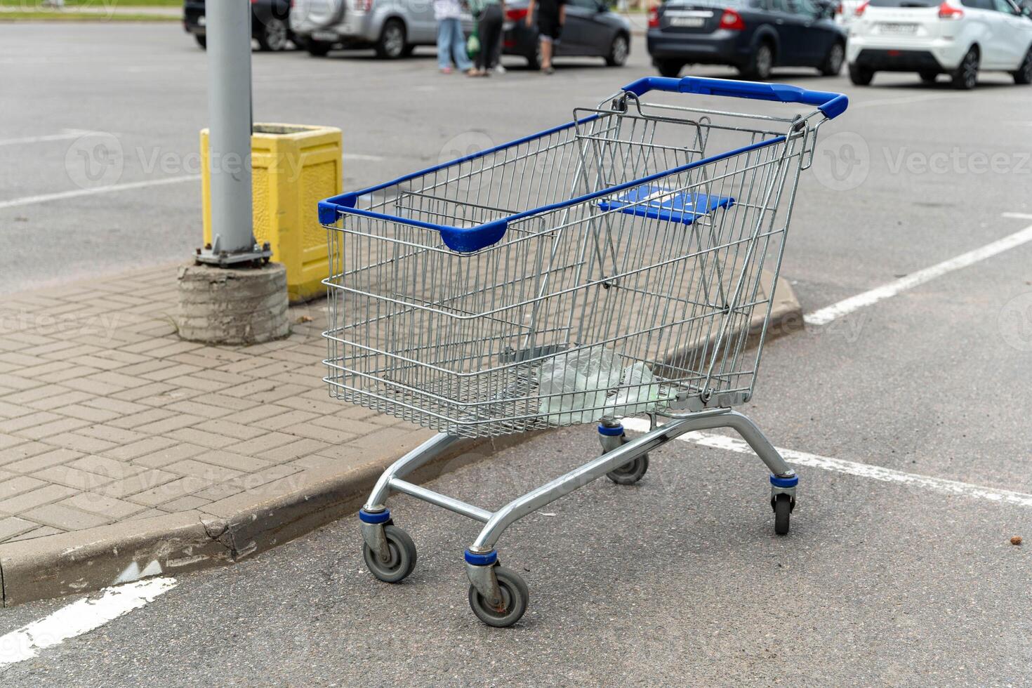 A shopping cart sits on the pavement, near a light pole, in a parking lot photo
