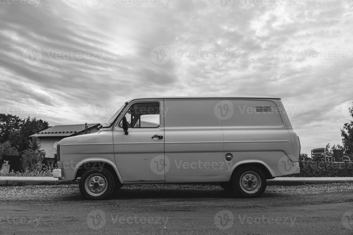 A classic white van is parked on a residential street under a cloudy sky photo