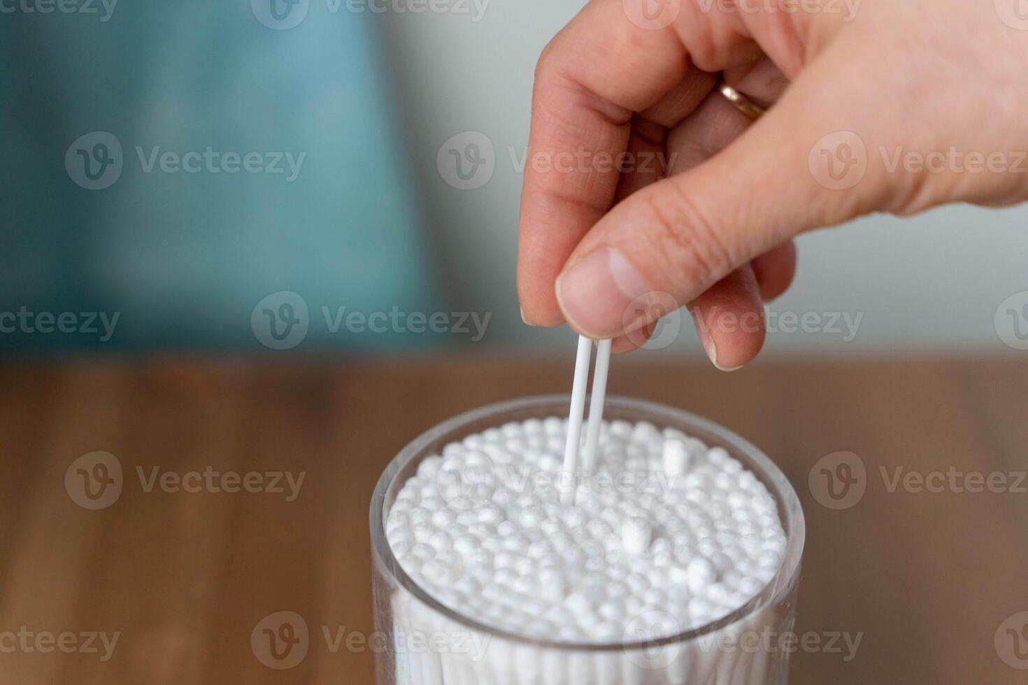 Woman's hand taking cotton swab from jar for personal hygiene and health care routine photo