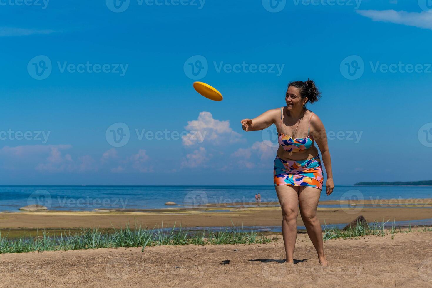 Woman throwing a frisbee on a sandy beach on a sunny day. body positive photo