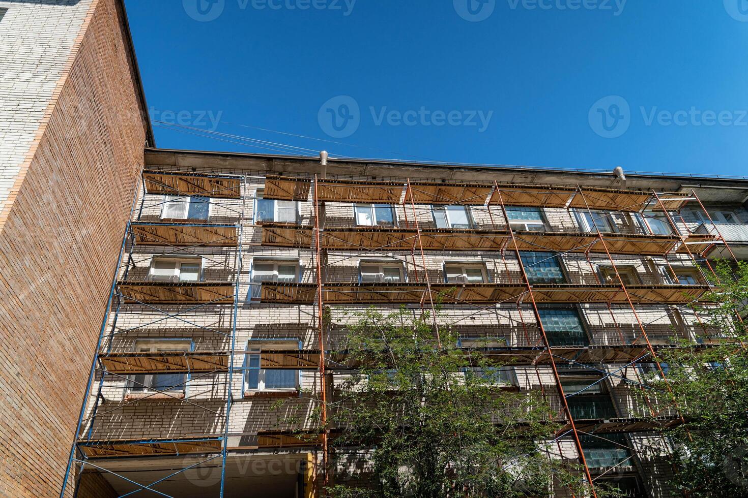 A brick building is covered in scaffolding against a bright blue sky photo