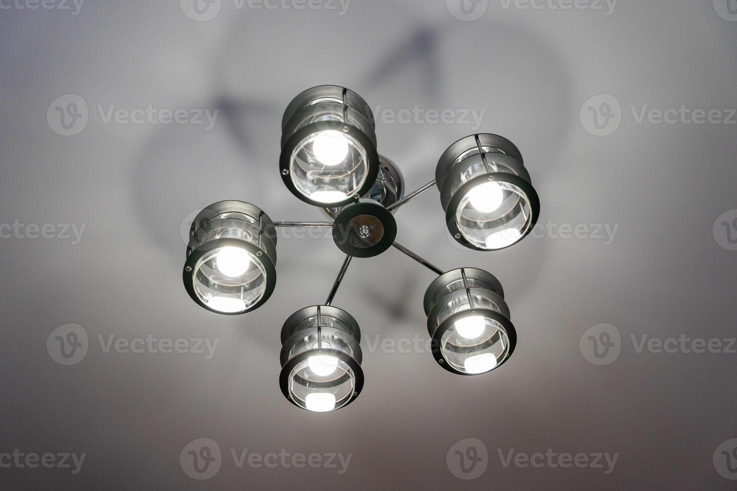 A modern black chandelier with five lights hangs from a white ceiling photo