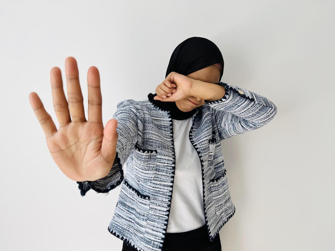 A young Muslim Asian woman feed sad hiding face with hand and putting other hand up to stop, gesture refusing isolated by white background photo