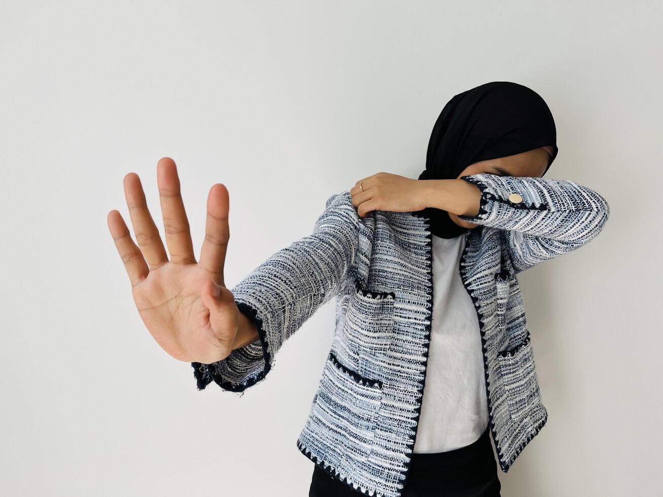 A young Muslim Asian woman hiding face with hand and putting other hand up to stop, gesture refusing isolated by white background photo