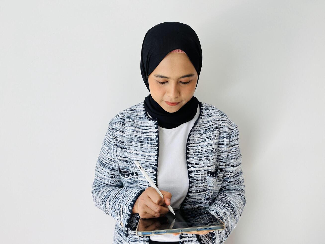 Smiling young Asian business woman wearing a black hijab, professional manager holding digital tablet computer using pen standing isolated by white background photo