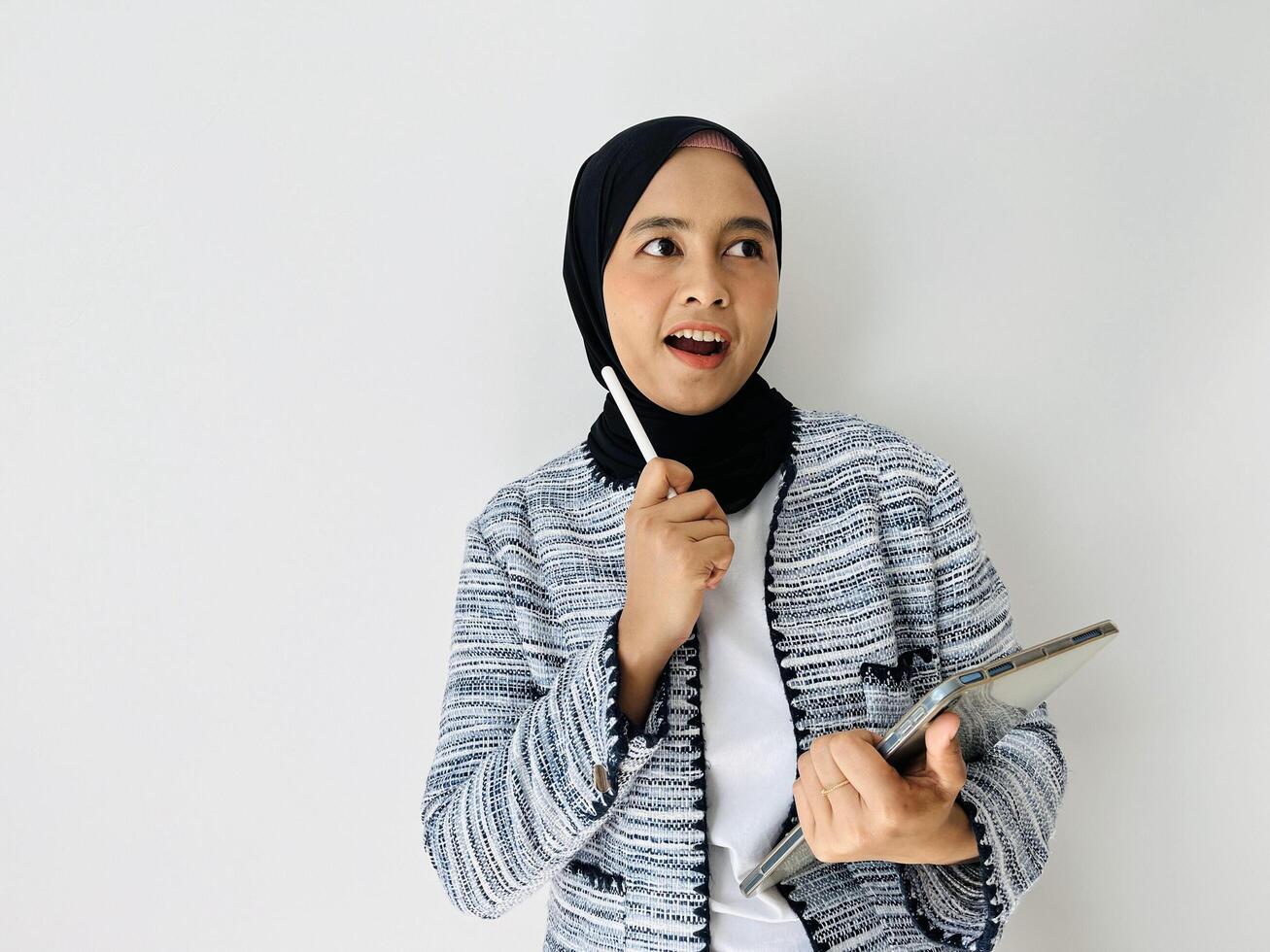 Portrait of happy young Muslim Asian woman got good ideas and looking up while holding mobile tablet. Got solution. Excited smart thoughtful, pointing up, eureka moment white background. photo