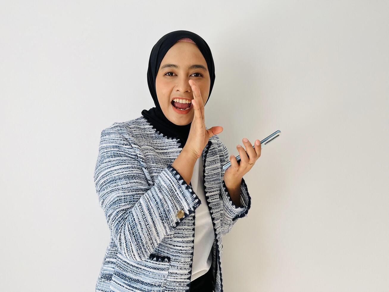 Surprised happy beautiful Asian woman hijab woman act like a telling something while hold mobile phone. Expressive facial expressions. Isolated on white background photo