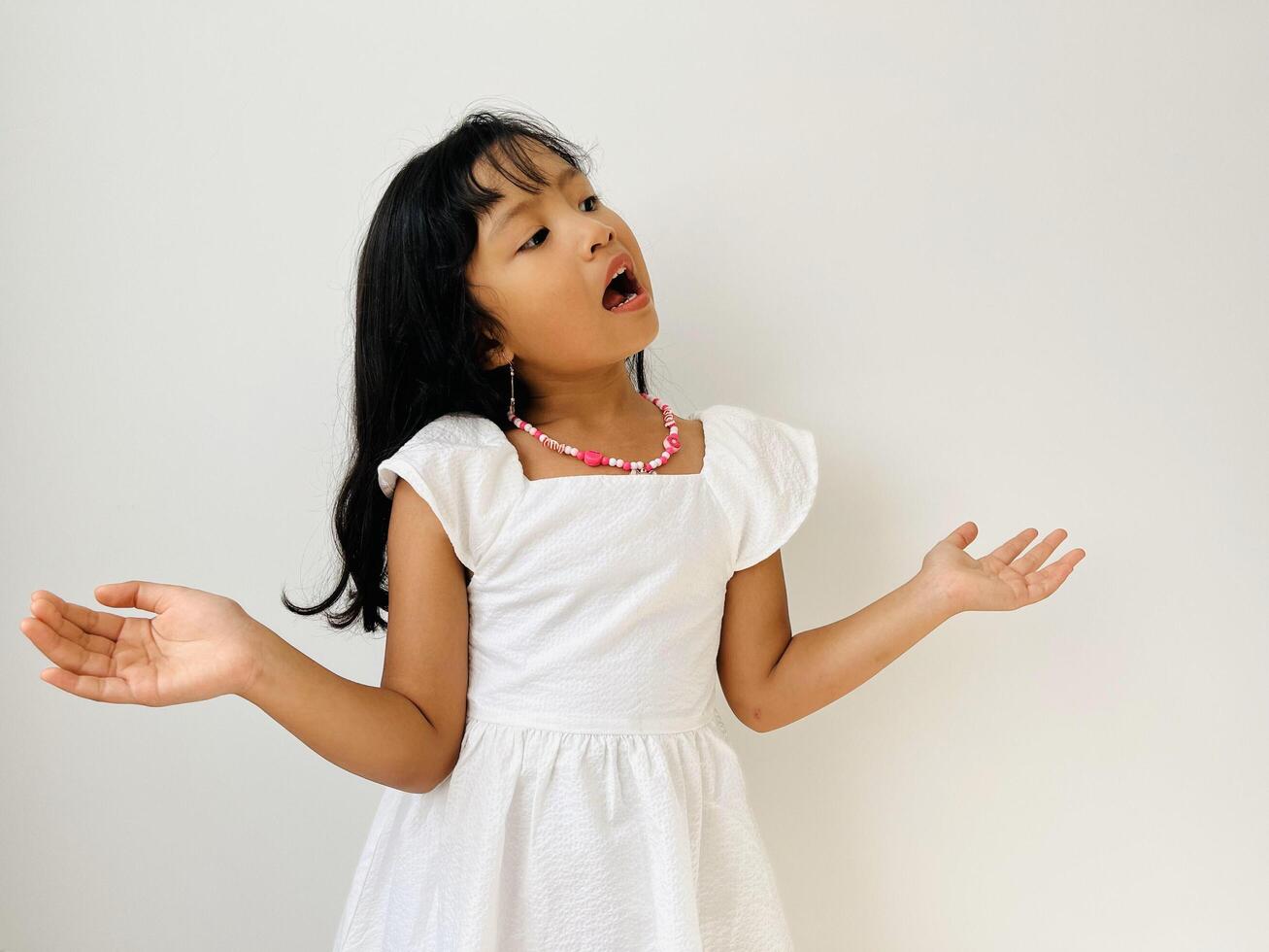 So what. Portrait of arrogant unbothered good looking modern little Asian girl, shrugging careless hands sideways smiling gasping indifferent, telling something obvious. photo