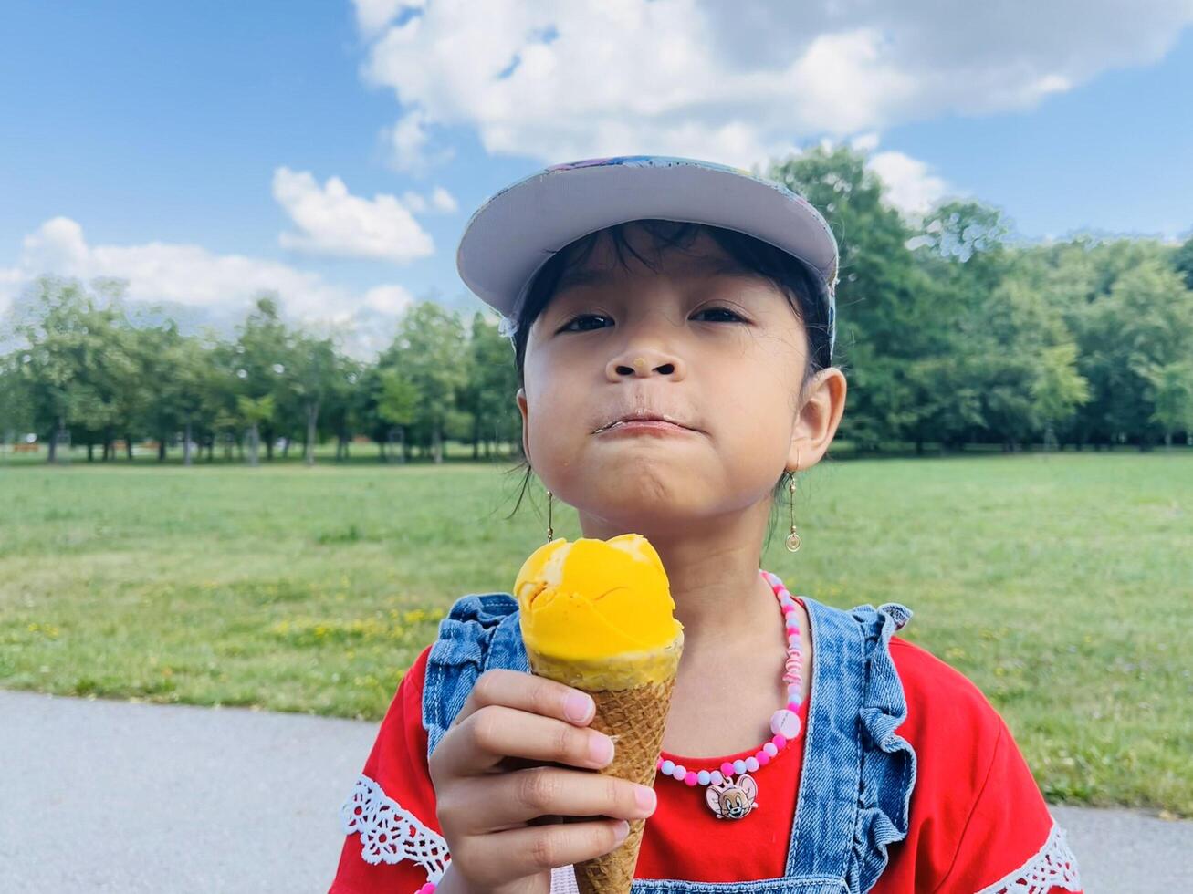 A five years old Asian child eats ice cream in the summer when it's hot outside. Mango Ice cream in a waffle cone. A happy and contented child in the park photo
