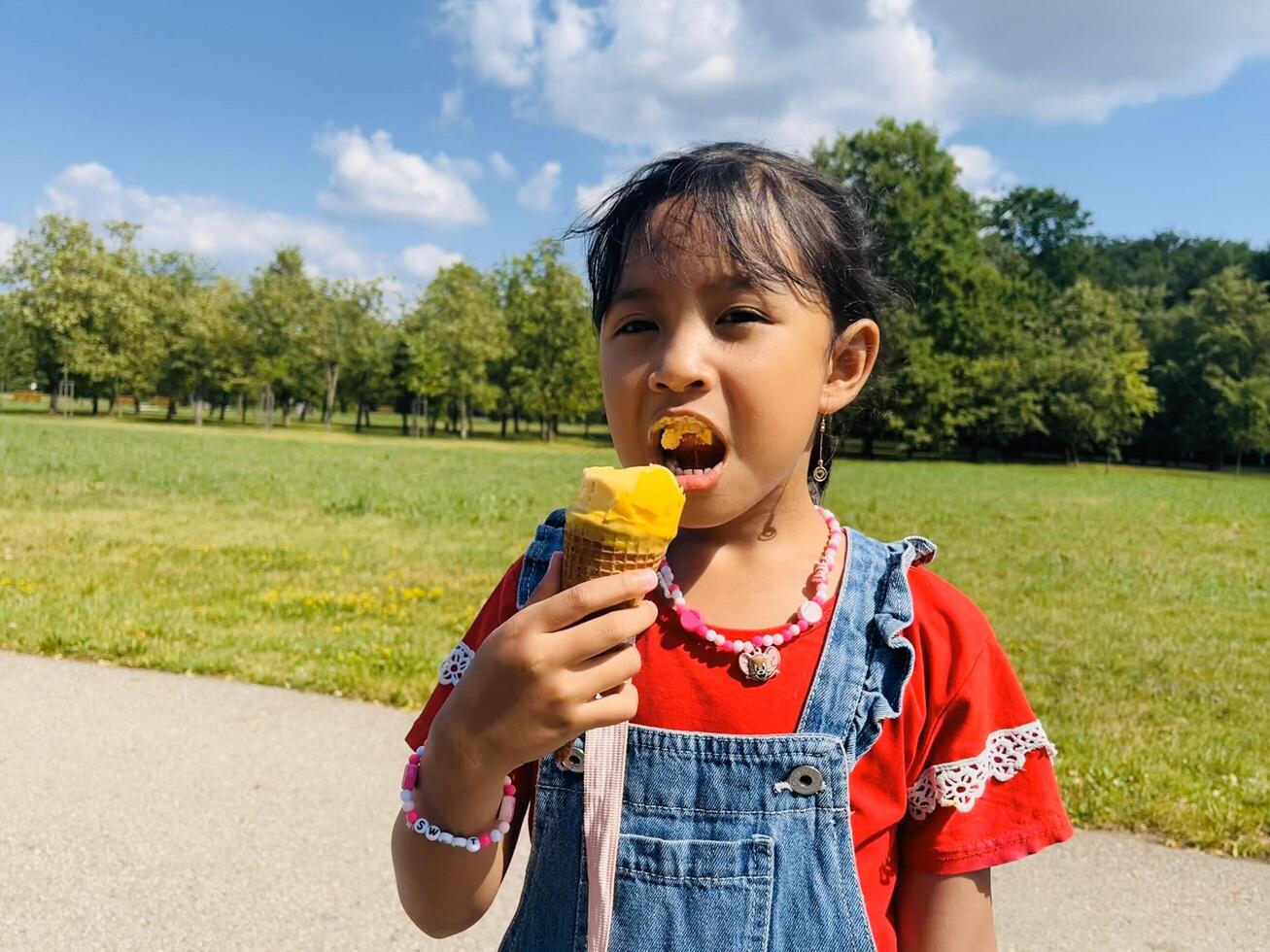 A five years old Asian child eats ice cream in the summer when it's hot outside. Mango Ice cream in a waffle cone. A happy and contented child in the park photo
